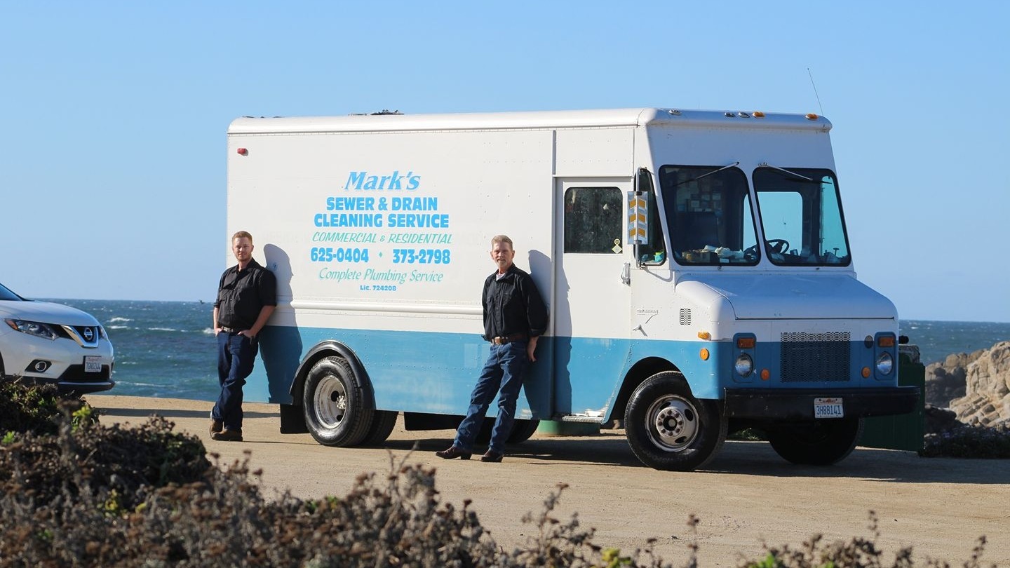 Mark and his father standing beside the Mark's Sewer & Drain Cleaning Service truck at the Monterey coast